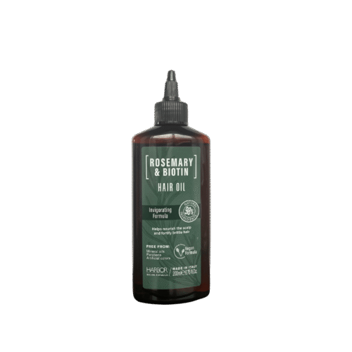 Glass bottle of Rosemary & Biotin Hair Oil made in Italy, with natural herbs and a wooden cap on a marble counter.